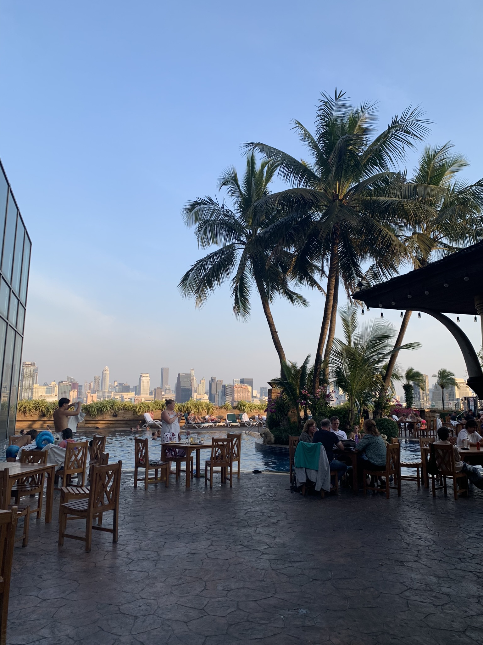 Uitzicht vanaf een sfeervol dakterras met palmbomen over de skyline van Bangkok