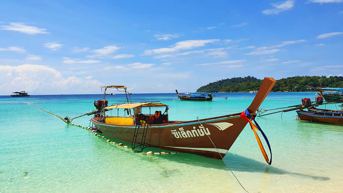 Een traditionele Thaise longtailboot drijvend op het turquoise water bij een van de stranden van Koh Lipe