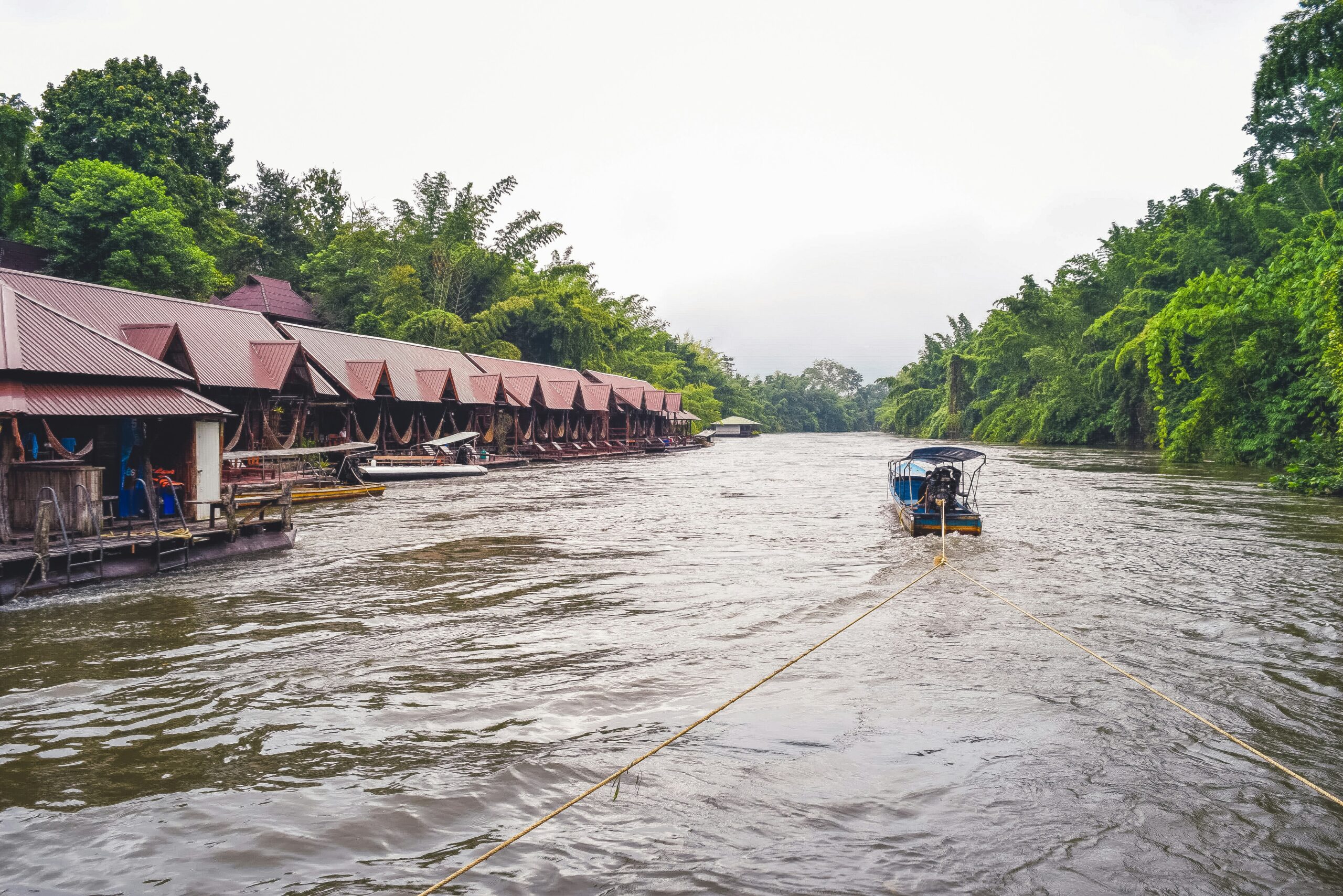 Een traditionele boot vaart over de River Kwai langs drijvende hotels in Kanchanaburi