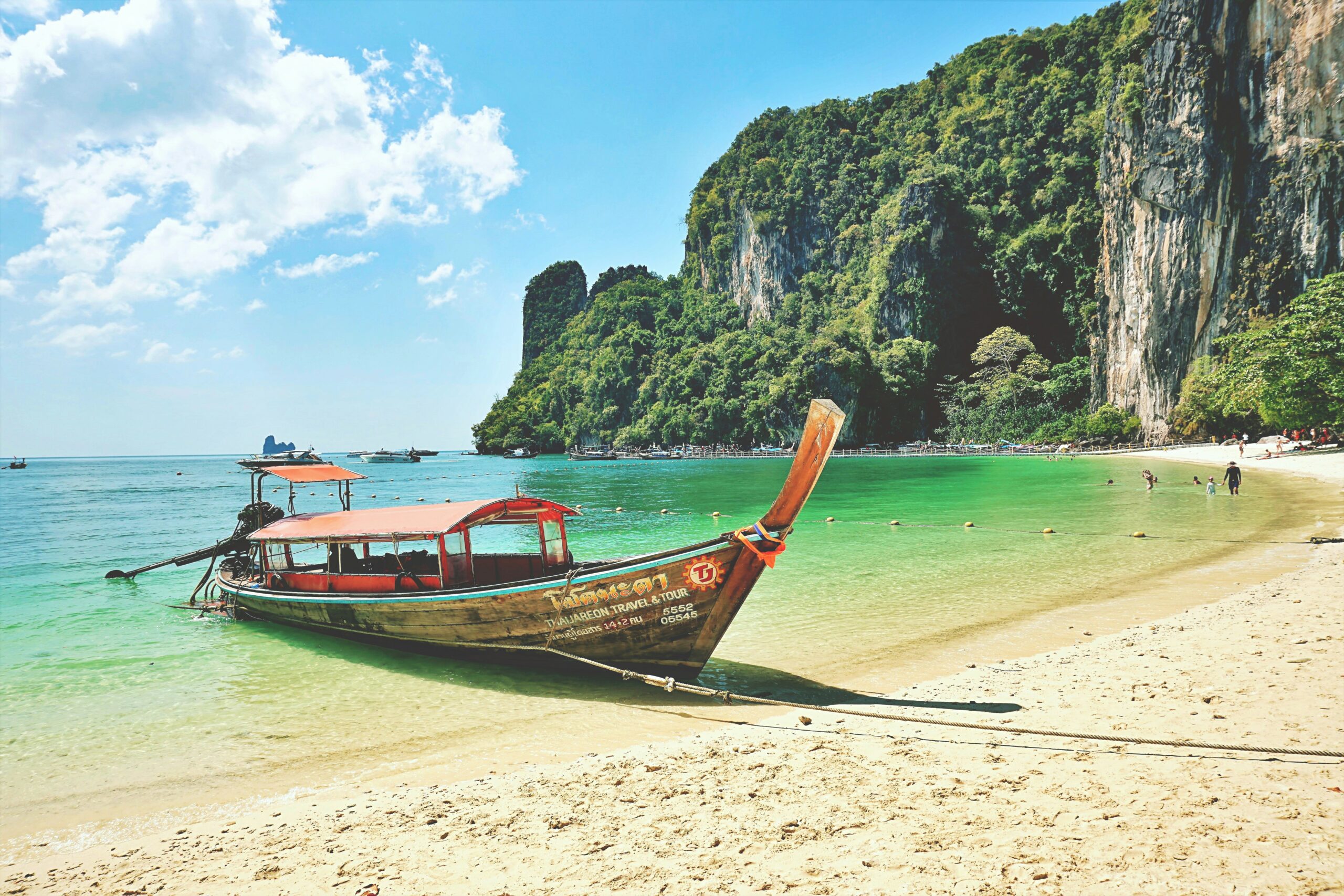 Traditionele houten longtailboot op het zandstrand van Ao Nang met de kenmerkende kalksteenrotsen van Krabi op de achtergrond