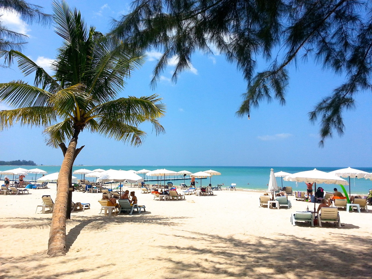 Prachtig breed wit zandstrand op Phuket met parasols en palmbomen onder een blauwe lucht