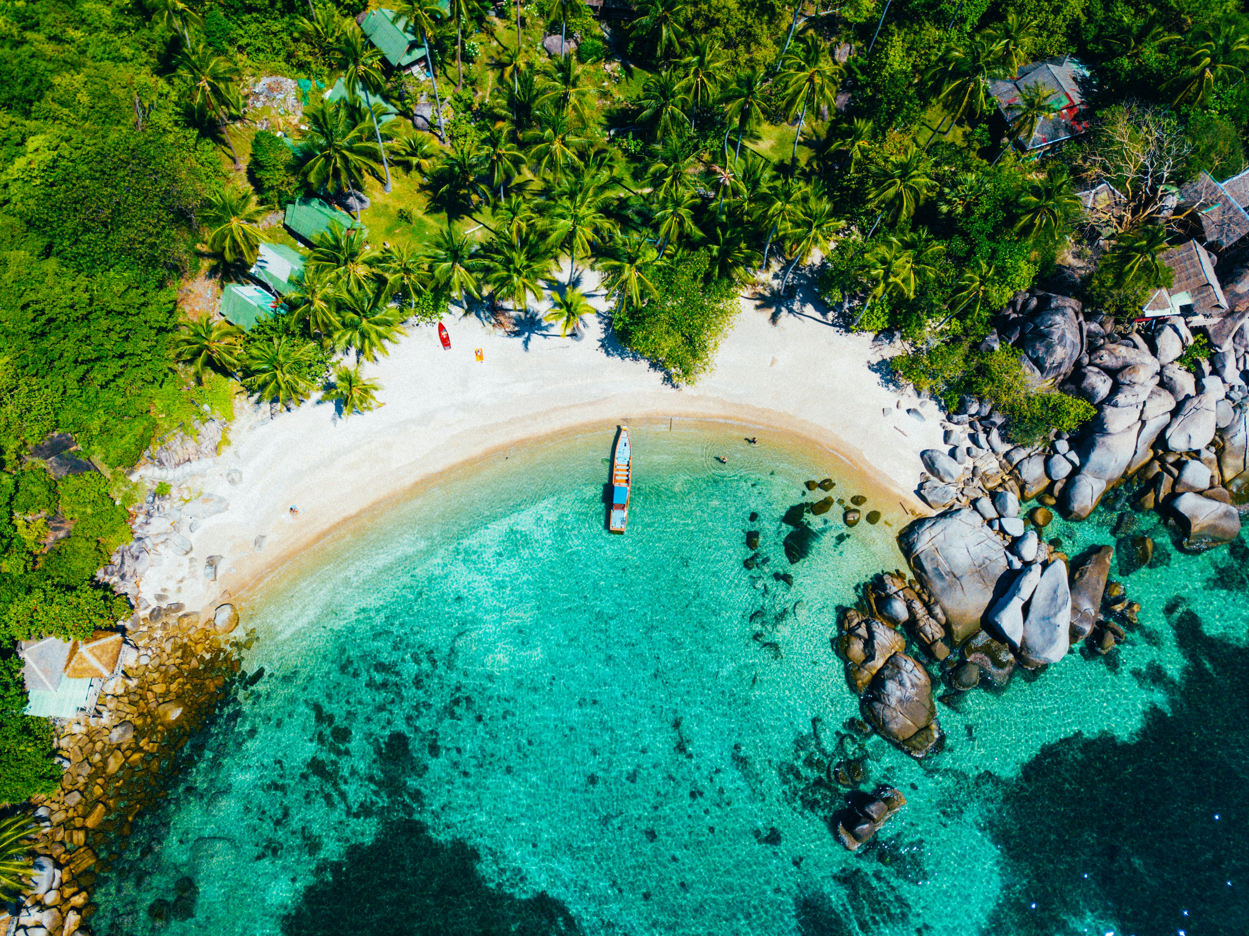 Luchtfoto van een idyllisch wit zandstrand met een houten bootje in het helderblauwe water van Koh Tao
