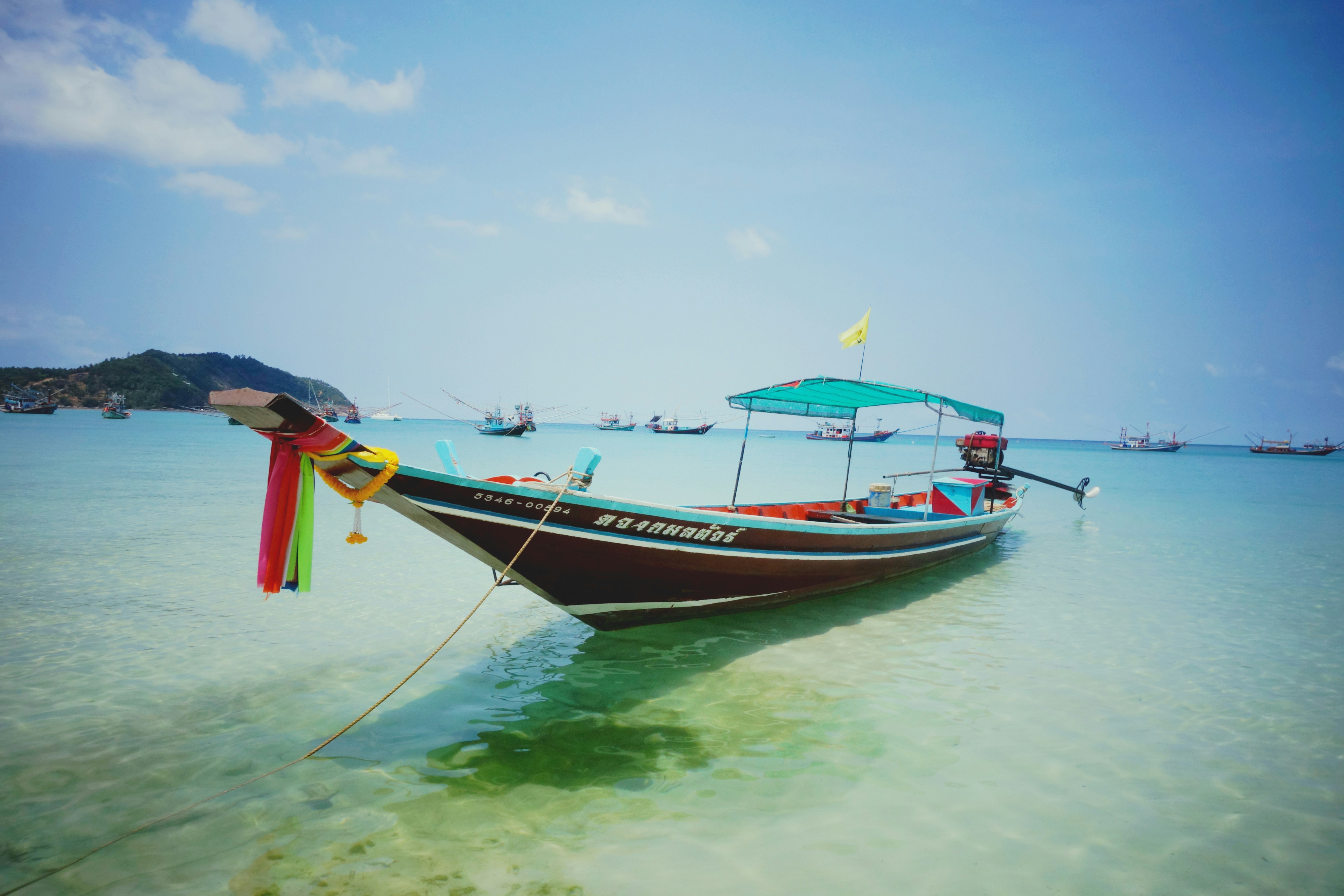 Traditionele houten longtailboot aangemeerd in het kristalheldere ondiepe water bij Koh Phangan